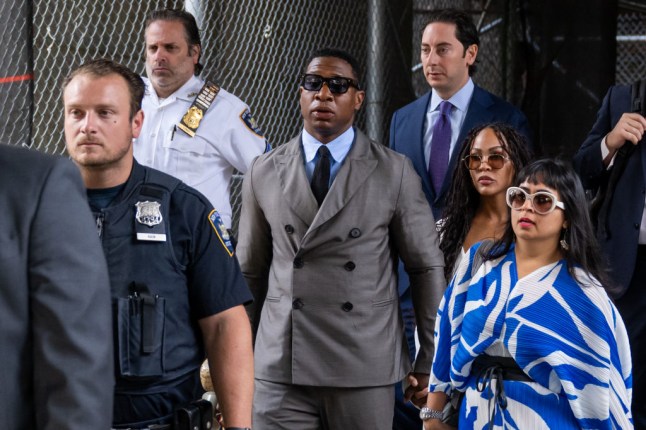 Jonathan Majors arriving at a court house in New York. He is wearing a grey suit with a pale blue shirt and a blue tie