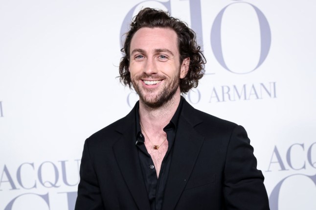 Aaron Taylor-Johnson at a red carpet event wearing a black shirt and smiling
