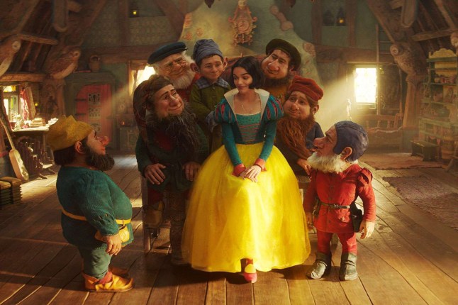 Rachel Zegler in Snow White sits surrounded by the seven dwarfs in their cottage