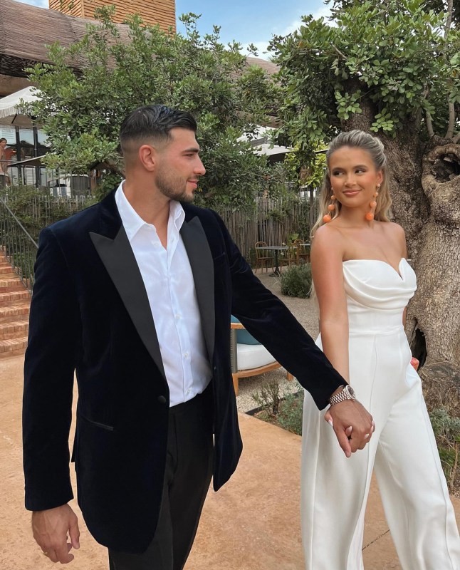 Molly-Mae Hague and Tommy Fury walk down pathway in suit and white jumpsuit