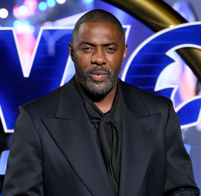 Idris Elba in black suit against blue background