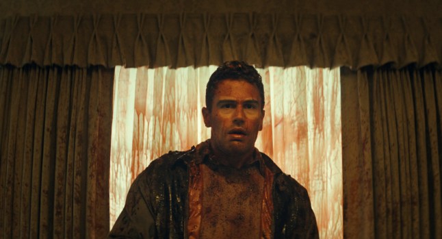 Theo James stands in front of blood covered curtains, covered in blood himself, in s scene from The Monkey