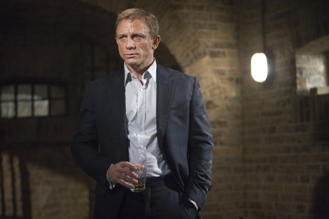 Daniel Craig as James Bond in Quantum Of Solace. He is wearing a black suit and standing in a brick wall room