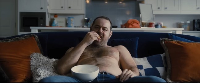 Danny Dyer as Jack sits topless on the sofa eating in a scene from Marching Powder