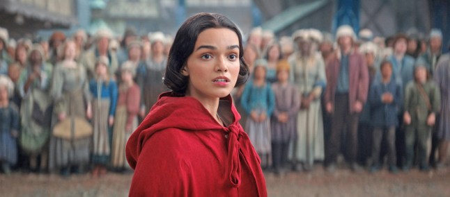 Rachel Zegler as Snow White stands in a red cloak in front of a crowd of people in a scene from Snow White