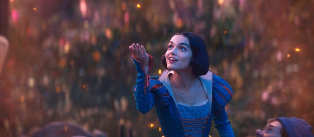 Rachel Zegler as Snow White holds out her hand to a dancing firefly in a still from Snow White