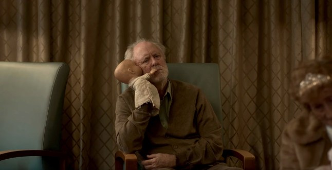 John Lithgow as Dave Crealy in The Rule of Jenny Pen. He is sat in a chair holding a hand puppet to his face