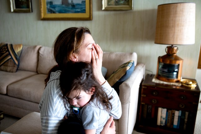 Tired mother and toddler hugging inside