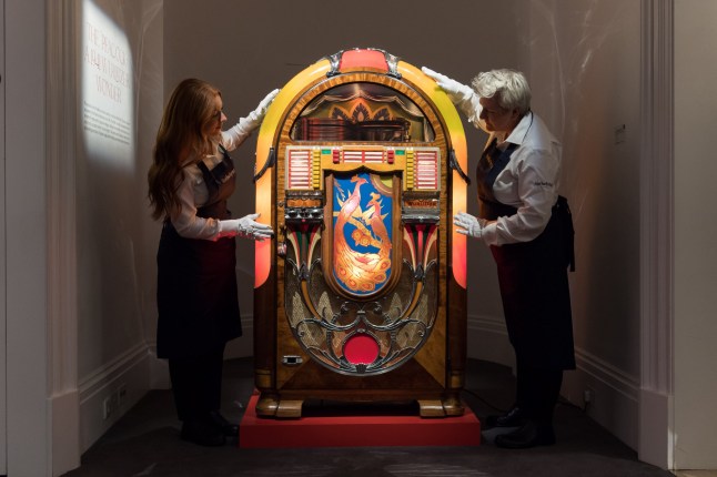 LONDON, UNITED KINGDOM - AUGUST 03: Art handlers pose with 1941 illuminated Wurlitzer jukebox (estimate ????15,000-25,000) during a photocall at Sotheby's auction house for the unveiling of Freddie Mercury's entire private collection ahead of an exhibition and six dedicated sales in London, United Kingdom on August 03, 2023. 'Freddie Mercury: A World of His Own' exhibition starring stage costumes, handwritten lyrics, fine and decorative arts, Japanese art, precious objects and a trove of personal belongings will be open to the public between August 4th and September 5th, before the items are offered across six dedicated auctions, each one devoted to a different aspect of Mercury??s life, both public and private. (Photo by Wiktor Szymanowicz/Anadolu Agency via Getty Images)