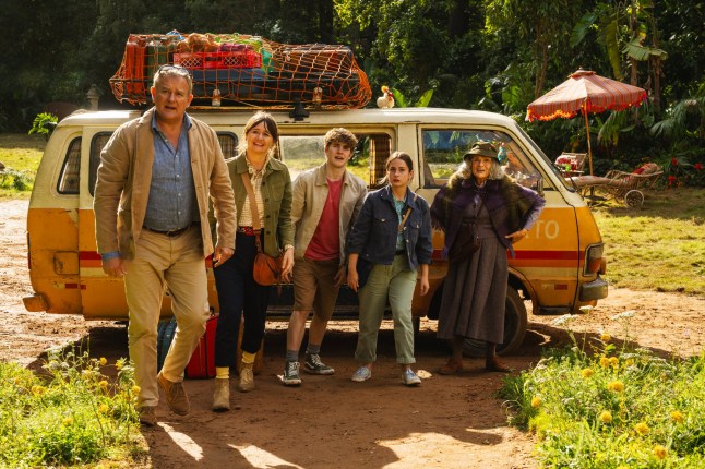 (L-R) Hugh Bonneville as Henry Brown, Emily Mortimer as Mary Brown, Samuel Joslin as Jonathan Brown, Madeleine Harris as Judy Brown, Julie Walters as Mrs. Bird all stand in front of a minivan in holiday outfits in Paddington in Peru