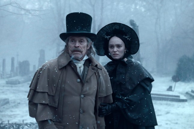 Willem Dafoe as Prof. Albin Eberhart von Franz in a top hat and overcoat, and Lily-Rose Depp in a black bonnet and cloak, stand together looking shocked in a snowy cemetery in Nosferatu