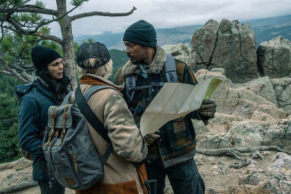 Morena Baccarin, Maddie Hasson and Anthony Mackie look at a map as they stand on a rocky outcrop in a scene from Elevation