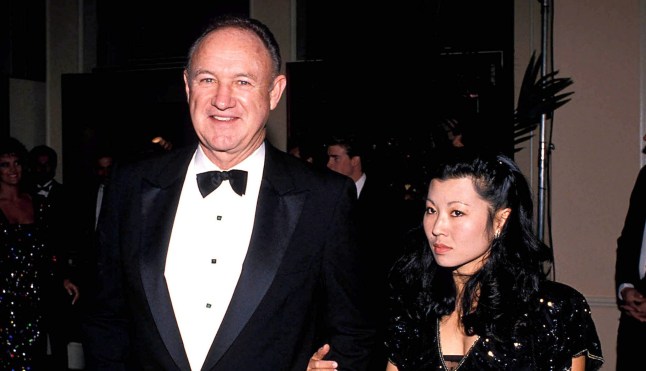 Genen Hackman and Betsy Arakawa at a red carpet event. Gene is wearing a black tuxedo while Betsy is wearing a black dress