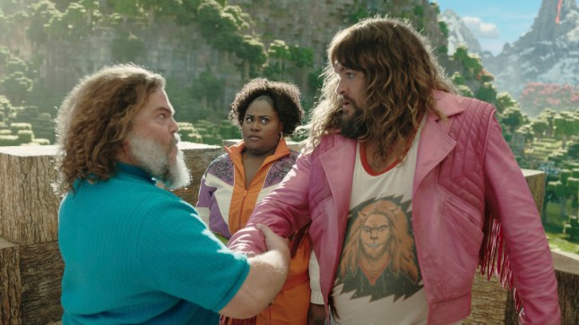 Jack Black and Jason Momoa grab each other's arms in a brotherly handshake as Danielle Brooks looks on from behind in a scene from A Minecraft Movie