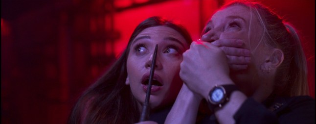 Allison Pittel as Selena holding a knife and Amy Schumacher as EMT Amber holding her hands over her mouth, both looking terrified, in Screamboat