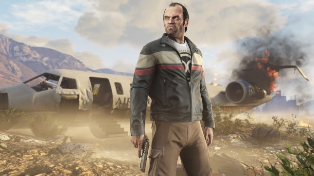 GTA 5 protagonist Trevor holding a pistol while standing in front of a burning wrecked plane.