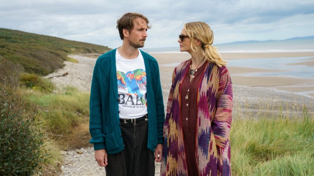 (L to R) Tom Basden as Herb McGwyer and Carey Mulligan as Nell Mortimer look at each other while standing on a beach in The Ballad of Wallis Island