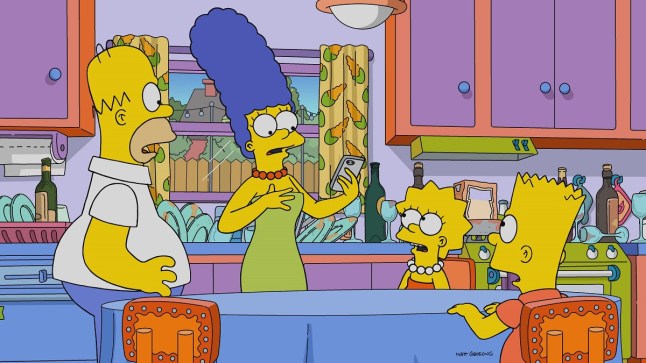 The Simpson family in their kitchen looking shocked at a mobile phone in Marge's hand